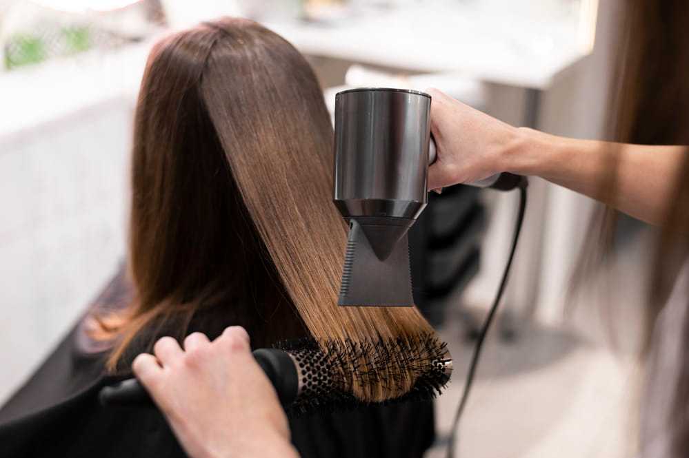 Hairdresser blow-drying and styling straight brown hair with a round brush.