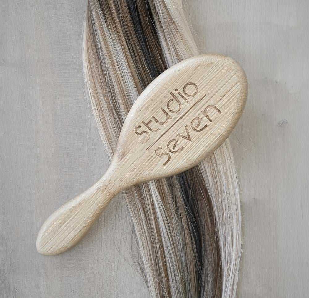 Wooden hairbrush on blonde and brown hair strands labeled "Studio Seven.